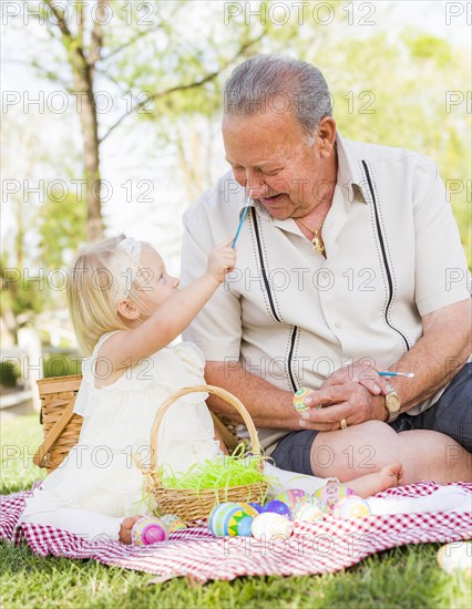 Loving grandfather and granddaughter coloring easter eggs together on picnic blanket at the park