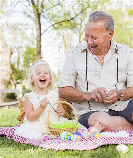 Loving grandfather and granddaughter coloring easter eggs together on picnic blanket at the park