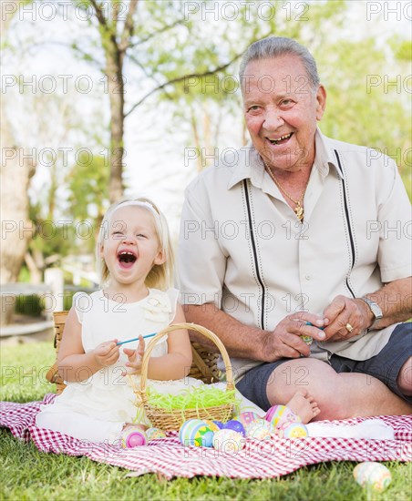 Loving grandfather and granddaughter coloring easter eggs together on picnic blanket at the park