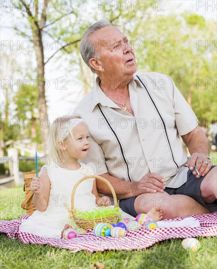 Loving grandfather and granddaughter coloring easter eggs together on picnic blanket at the park