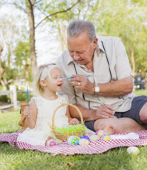 Loving grandfather and granddaughter coloring easter eggs together on picnic blanket at the park