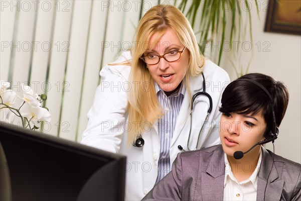 Female doctor discusses work on computer with receptionist assistant in an office setting