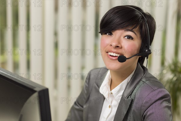 Attractive young mixed-race woman smiles wearing headset near computer monitor