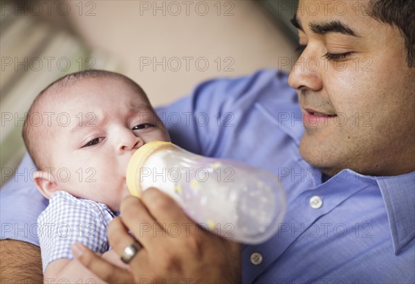 Happy hispanic father bottle feeding his very content son