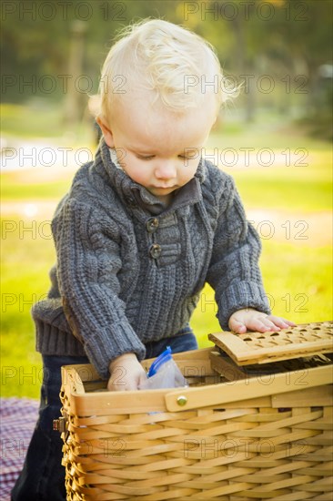 Adorable little blonde baby boy opening a picnic basket outdoors at the park