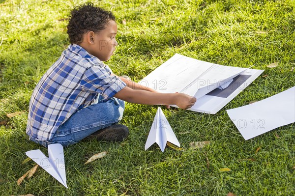 mixed-race boy learning how to fold paper airplanes outdoors on the ...