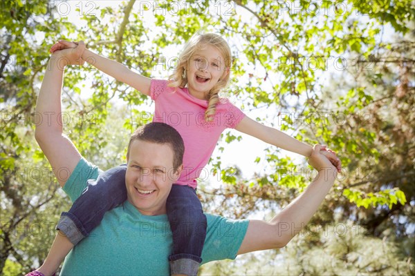 Cute young girl rides piggyback on her dads shoulders outside at the park