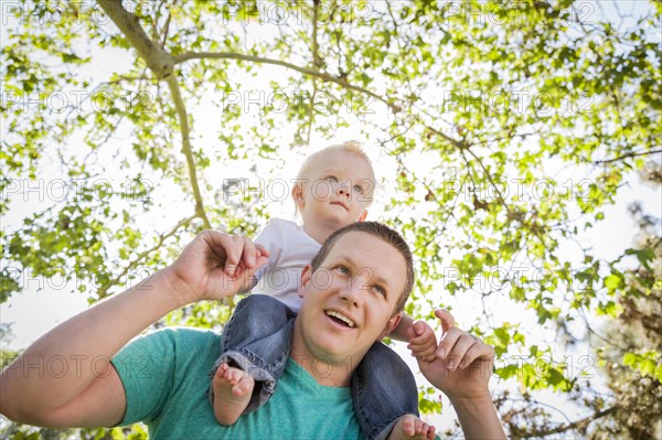 Cute young boy rides piggyback on his dads shoulders outside at the park