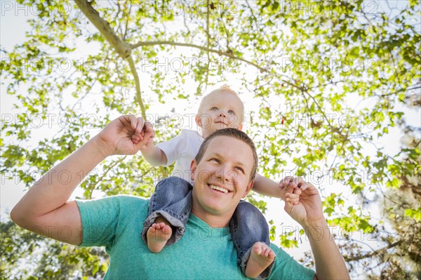 Cute young boy rides piggyback on his dads shoulders outside at the park