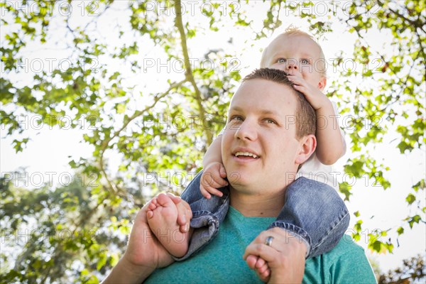 Cute young boy rides piggyback on his dads shoulders outside at the park
