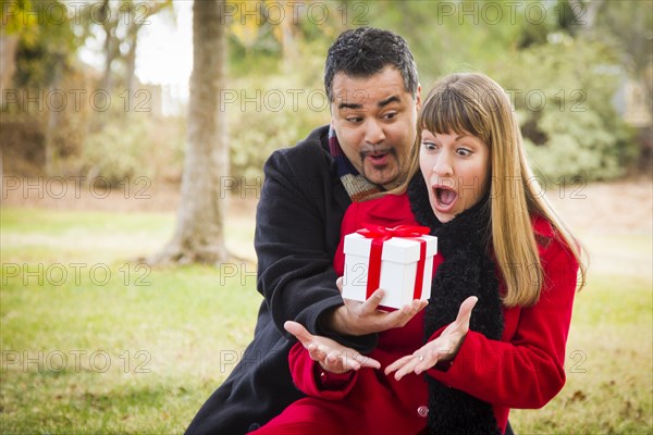 Young attractive mixed-race couple sharing christmas or valentines day gift in the park
