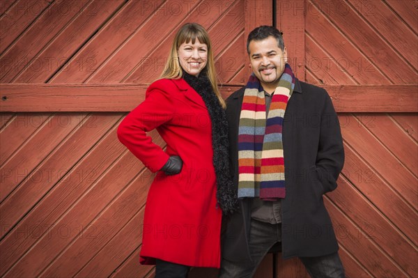 Young mixed-race couple portrait in winter clothing against barn door