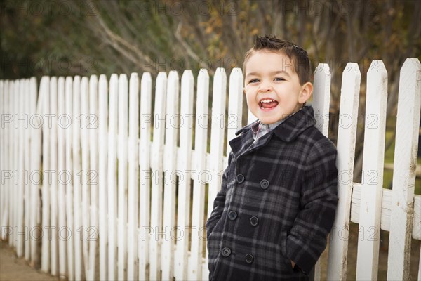 Young mixed-race boy calling out to friends waiting for school bus along fence outside