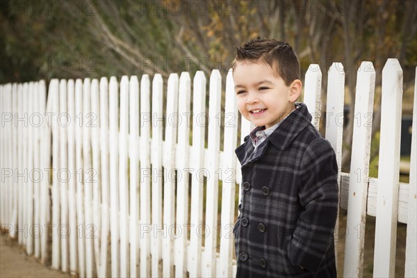 Young mixed-race boy waiting for school bus along fence outside