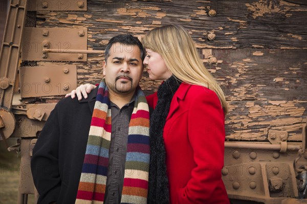 Young mixed-race couple portrait in winter clothing against side of rustic train