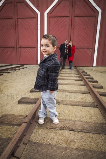 Young adorable mixed-race boy at train depot with parents smiling behind