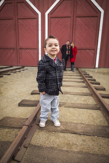 Young adorable mixed-race boy at train depot with parents smiling behind