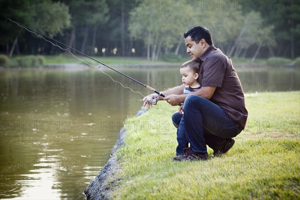 Happy young ethnic father and son fishing at the lake