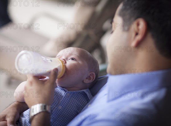 Happy hispanic father bottle feeding his very content mixed-race son