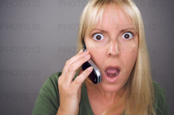 Stunned blond woman using cell phone against a grey background