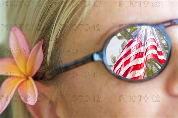Girl with plumeria flower in hair and wearing sunglasses with reflection of american flag and palm trees