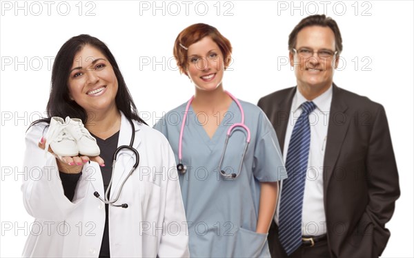 Attractive hispanic female doctor or nurse holding out baby shoes and support staff behind isolated on a white background