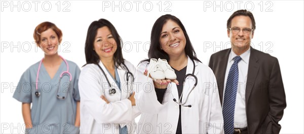 Attractive hispanic female doctor or nurse holding out baby shoes and support staff behind isolated on a white background