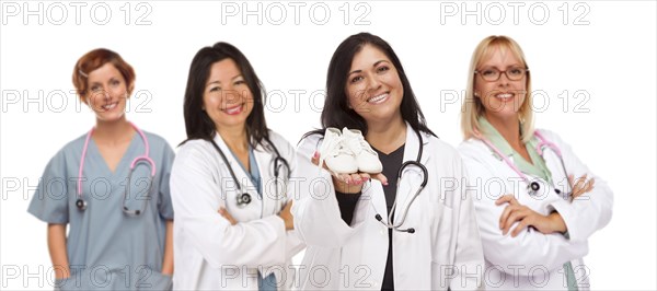 Attractive hispanic female doctor or nurse holding out baby shoes and support staff behind isolated on a white background