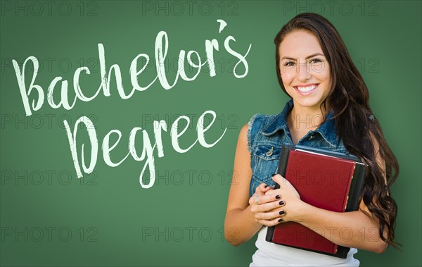 Bachelors degree written on chalk board behind mixed-race young girl student holding books