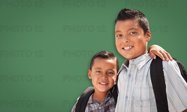 Cute hispanic boys wearing backpacks in front of blank chalk board