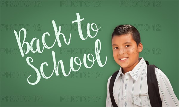 Cute hispanic boy wearing A backpack in front of chalk board with back to school written on it