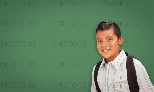 Cute hispanic boy with backpack in front of blank chalk board