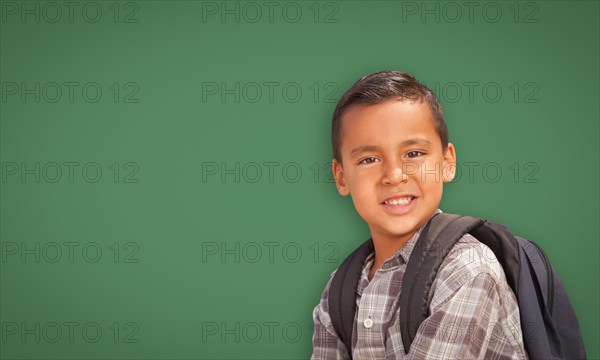 Cute hispanic boy with backpack in front of blank chalk board