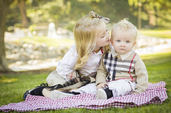 Sweet little girl kisses her baby brother on his cheek outdoors at the park
