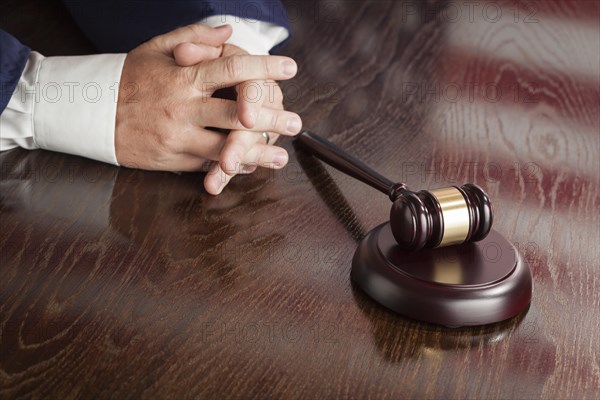 Male judge rests folded hands behind gavel with american flag reflection on wooden table