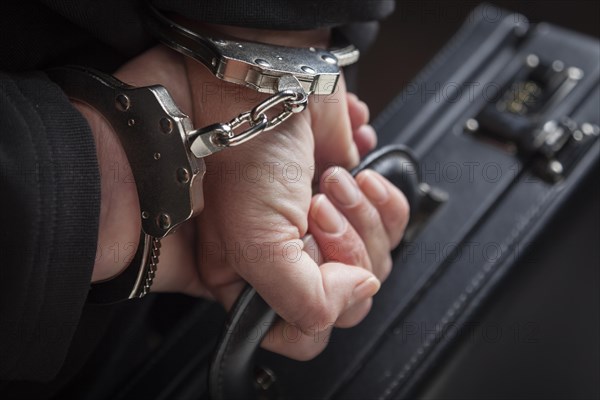 Woman wearing handcuffs carrying briefcase in dramatic lighting