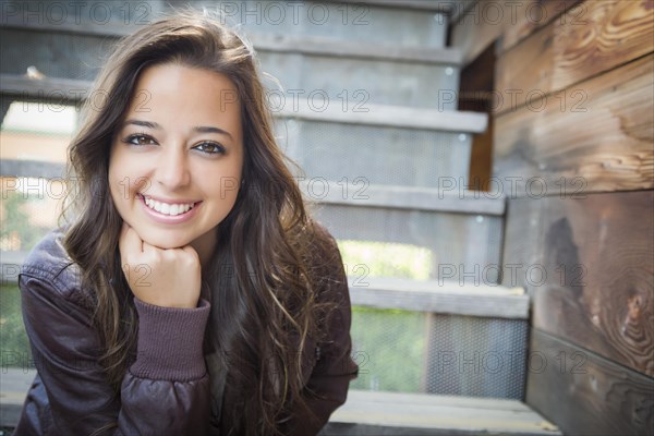 Portrait of a pretty mixed-race young adult woman sitting on a staircase wearing leather boots and jacket