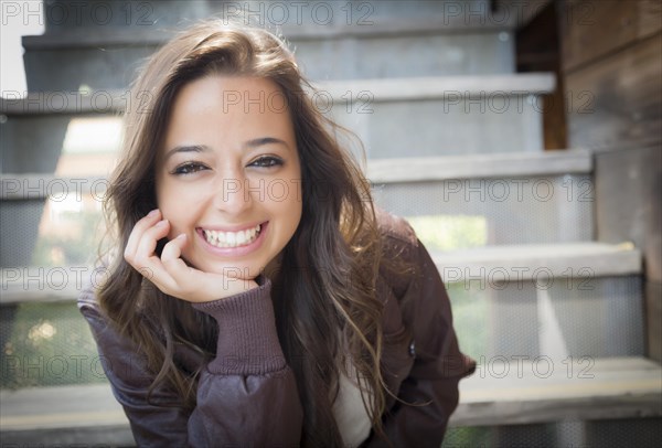 Portrait of a pretty mixed-race young adult woman sitting on a staircase wearing leather boots and jacket