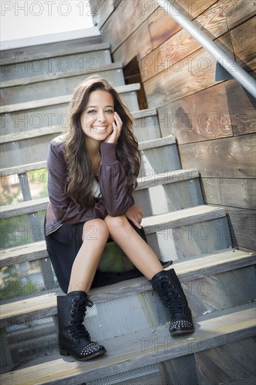 Portrait of a pretty mixed-race young adult woman sitting on a staircase wearing leather boots and jacket