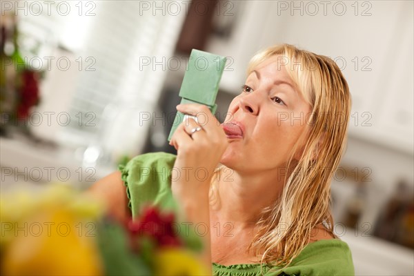 Blonde woman sticking her tongue out at herself in a compact mirror