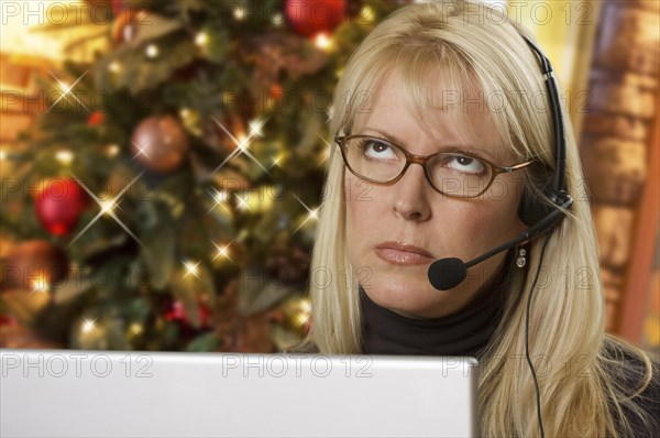 Upset woman with phone headset in front of christmas tree and computer screen
