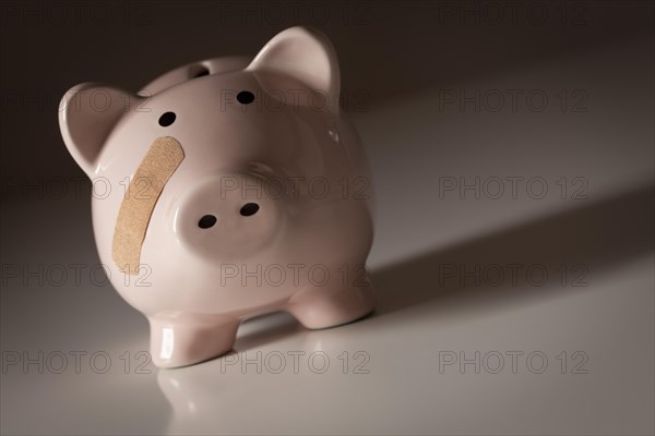 Piggy bank with bandage on face on gradated background