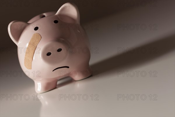 Piggy bank with bandage on face on dramatic gradated background