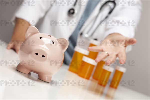 Doctor wearing stethoscope reaches palm out behind medicine bottles and piggy bank