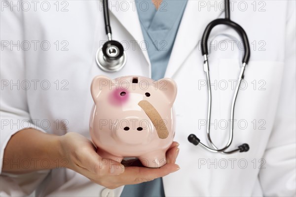 Female doctor with stethoscope holding piggy bank with bruised eye and bandage