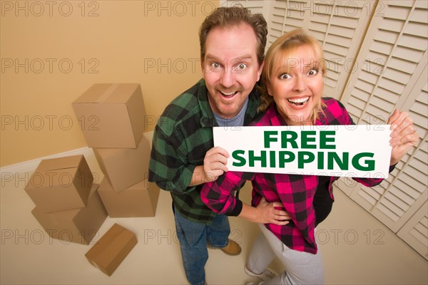 Goofy couple holding free shipping sign in room with packed cardboard boxes