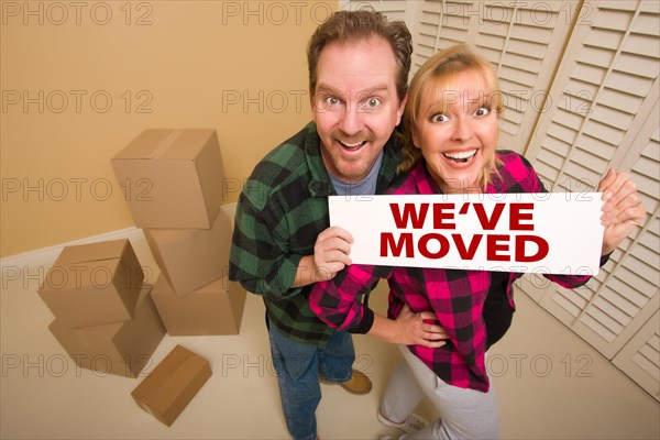 Goofy couple holding we've moved sign in room with packed cardboard boxes