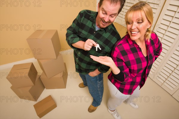 Goofy excited man handing keys to smiling wife in room with packed boxes