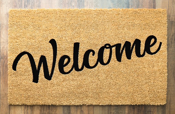 Tan welcome mat on wood floor background