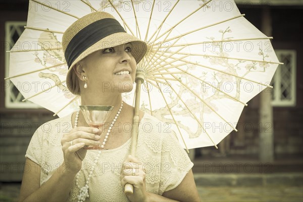 Beautiful 1920s dressed girl with parasol and glass of wine portrait